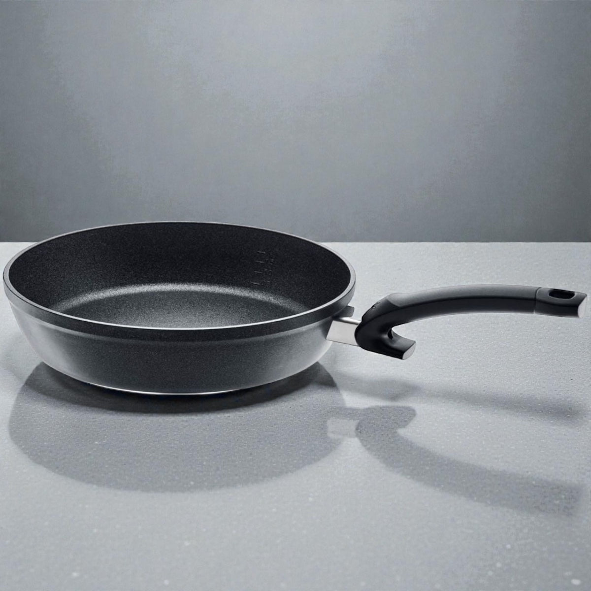 Tiefe schwarze Antihaft-Bratpfanne mit ergonomischem Griff auf grauer Oberfläche