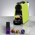 Kompakte grüne Kapsel-Kaffeemaschine mit Espresso in Glas und Nespresso-Kapseln auf Küchentisch – moderne Espressomaschine für Zuhause