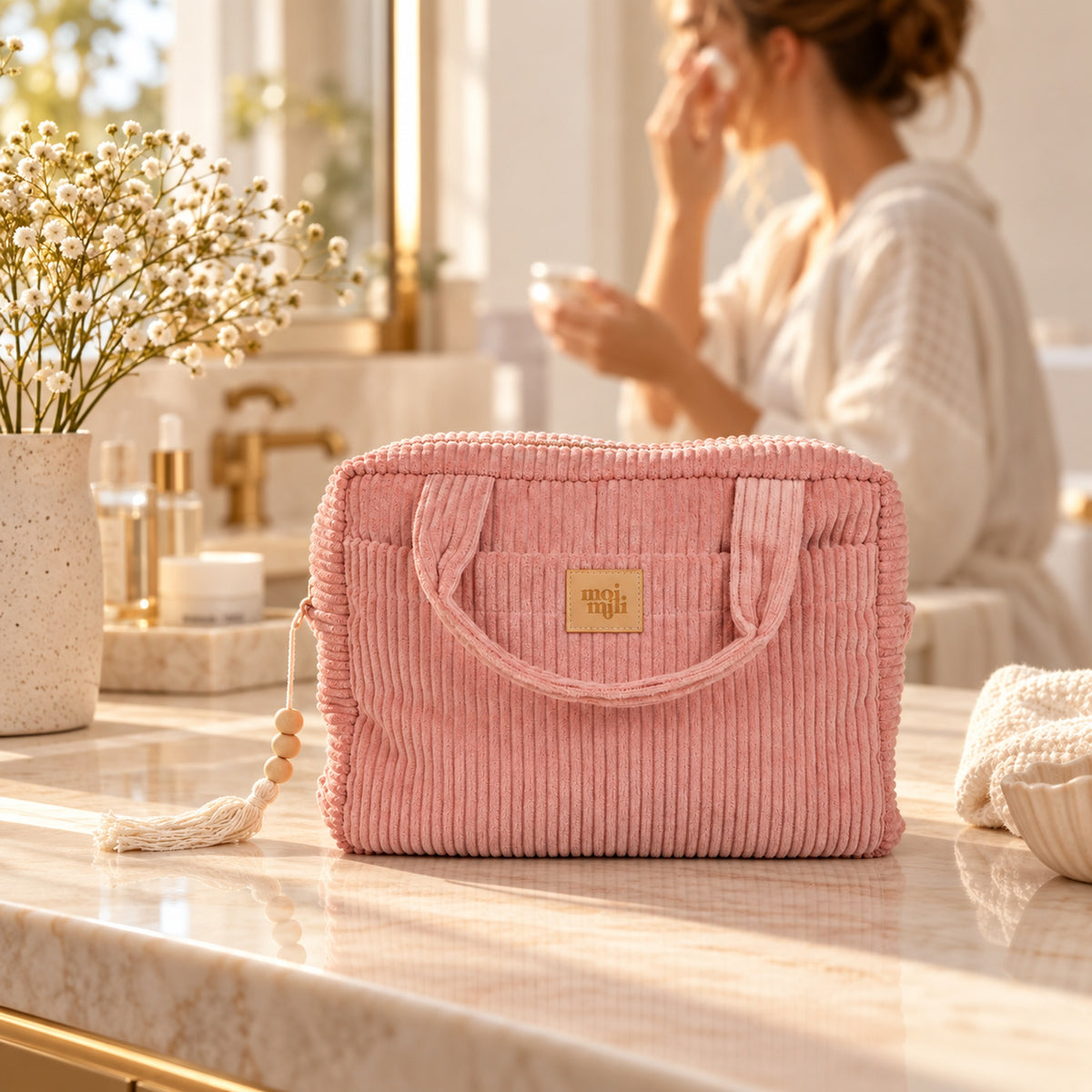 Große Kosmetiktasche Babyrosa aus rosa Cord auf einem hellen Waschtisch, Frau im Hintergrund