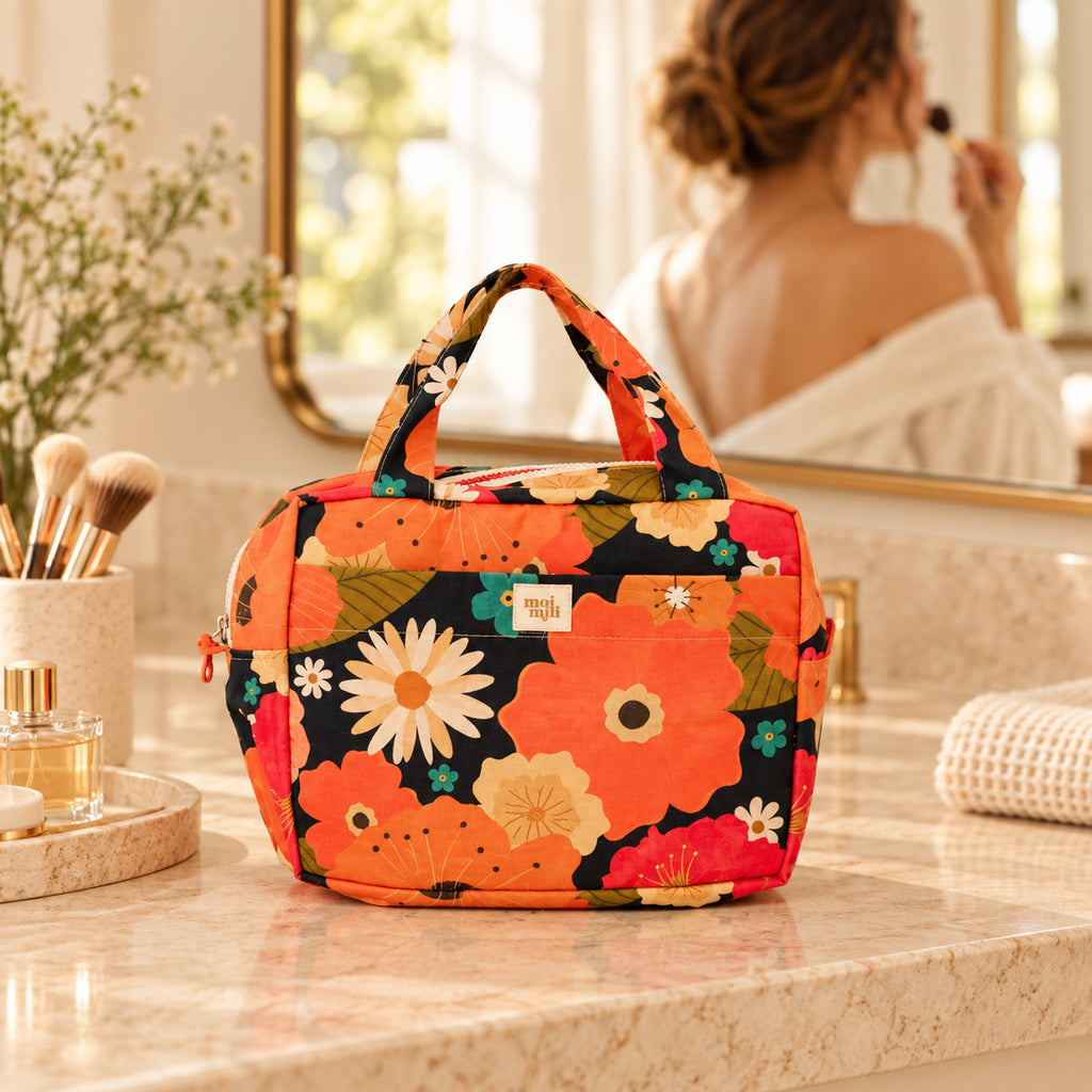 Große Kosmetiktasche Blumenpicknick mit orangefarbenem Blumenmuster auf hellem Waschtisch mit Frau im Hintergrund