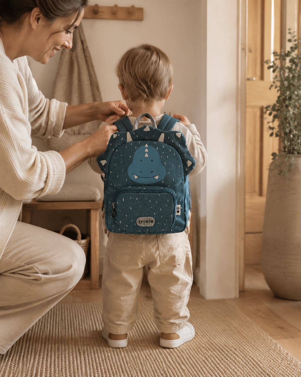 Mutter hilft Kleinkind mit Rucksack Mr. Triceratops