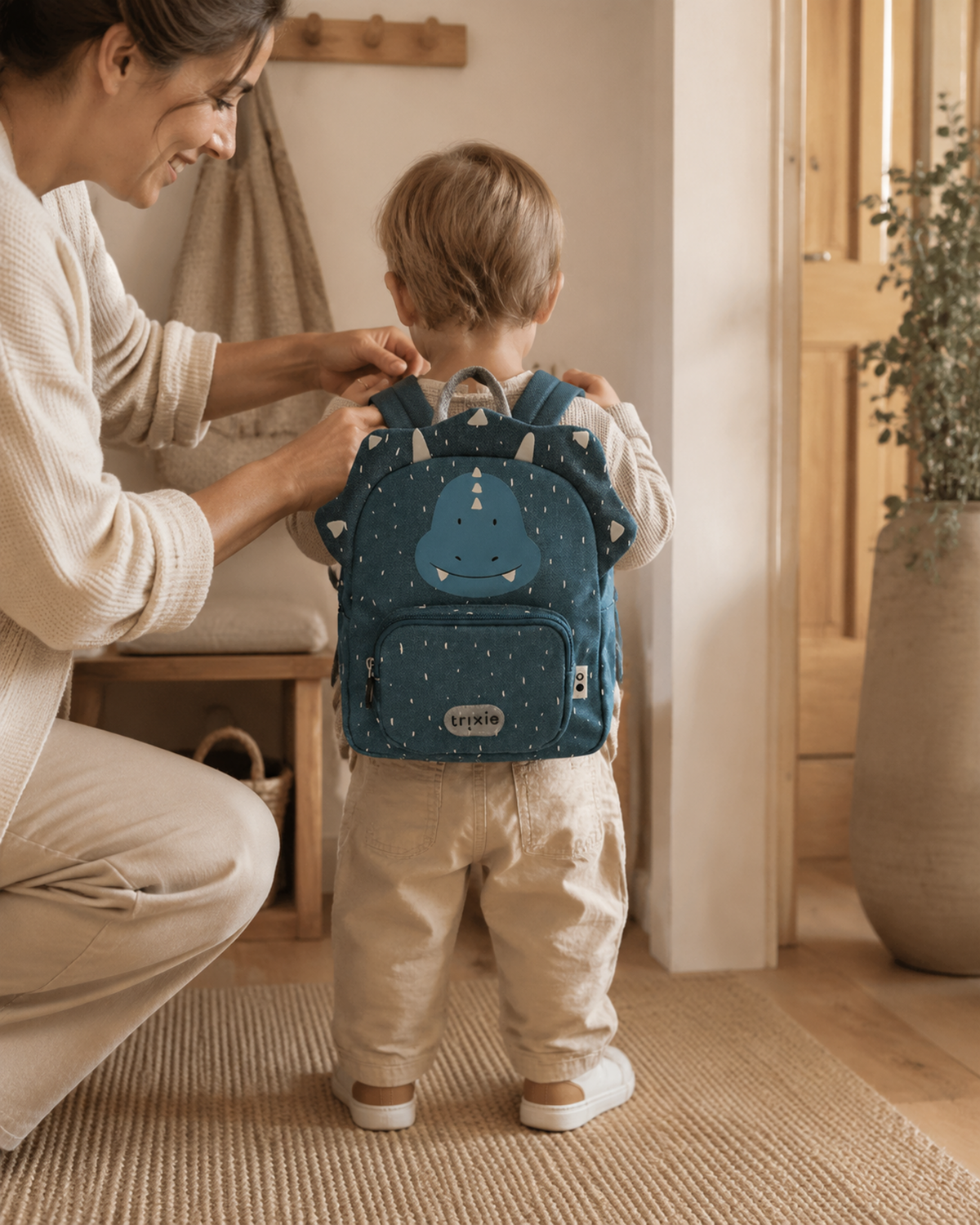 Mutter hilft Kleinkind mit Rucksack Mr. Triceratops